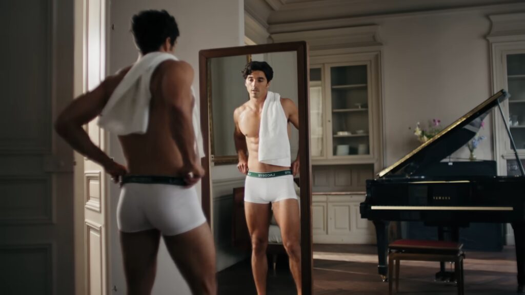 Taylor Zakhar Perez adjusting his Lacoste underwear in a sunlit Paris apartment