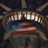 The image shows the head of the Statue of Liberty at night, with a person standing inside the crown's observation deck. A large Puerto Rican flag is draped over the statue's forehead, partially covering its eyes.