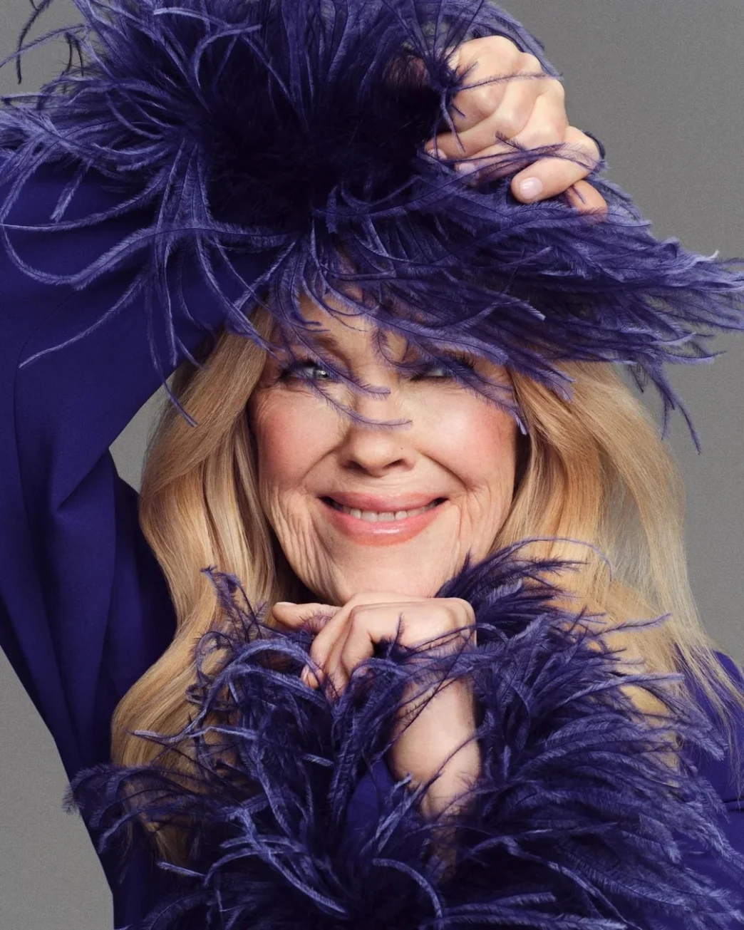 Catherine O’Hara by Jason Kim for Stylist in a lavender feathered outfit smiling.
