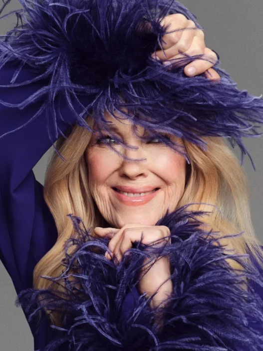 Catherine O’Hara by Jason Kim for Stylist in a lavender feathered outfit smiling.