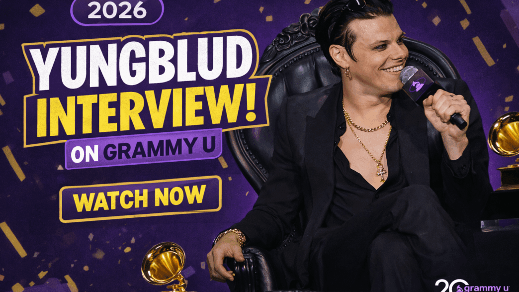YUNGBLUD speaks on stage during a GRAMMY U interview in 2026, seated in a black armchair and holding a microphone beside GRAMMY trophies.