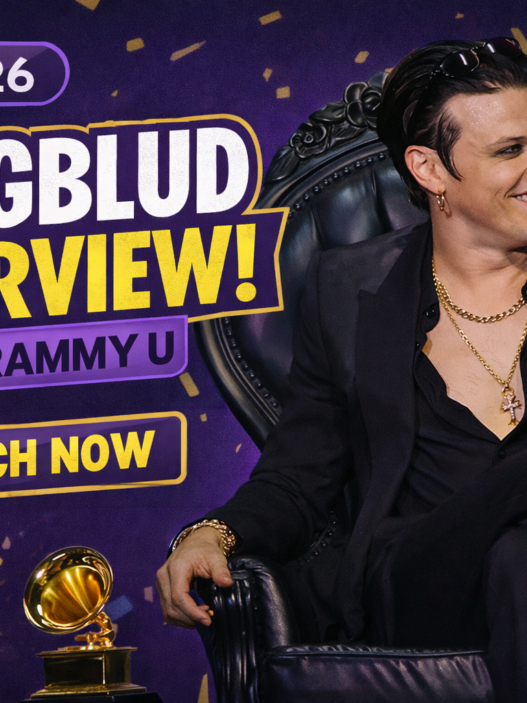 YUNGBLUD speaks on stage during a GRAMMY U interview in 2026, seated in a black armchair and holding a microphone beside GRAMMY trophies.