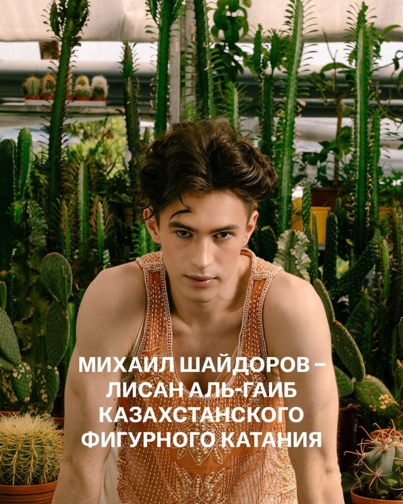 Mikhail Shaidorov stands in front of tall cacti and potted plants in a greenhouse, wearing a detailed beaded costume and looking directly at the camera. The words МИХАИЛ ШАЙДОРОВ — ЛИСАН АЛЬ-ГАИБ КАЗАХСТАНСКОГО ФИГУРНОГО КАТАНИЯTranslated:“Mikhail Shaidorov — the Lisan al‑Gaib of Kazakhstani figure skating.”It’s a Dune reference — “Lisan al‑Gaib” meaning “Voice from the Outer World,” often used to describe a prophesied or exceptional figure.