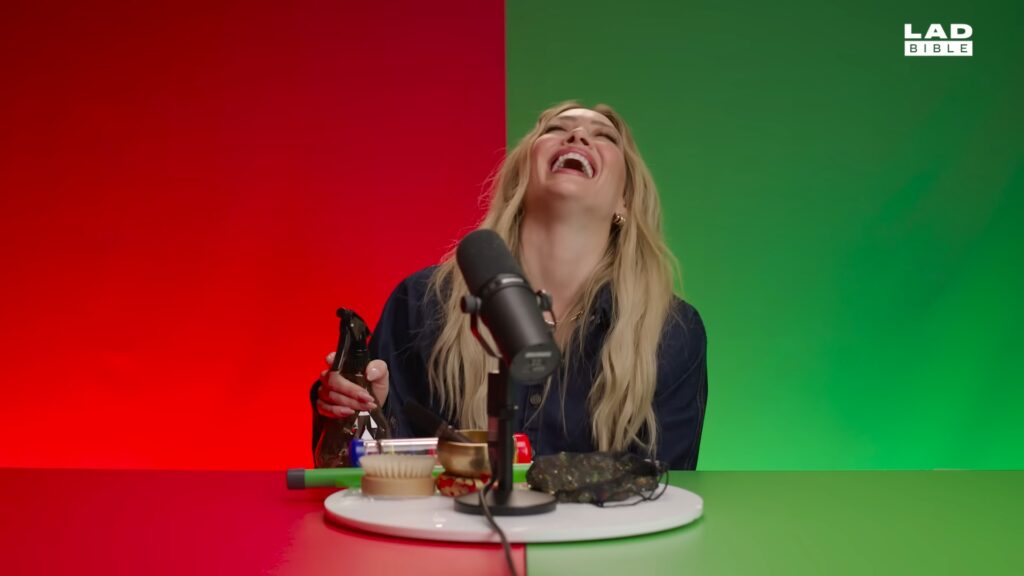 Hilary Duff laughing at a table surrounded by ASMR props during her Swipe Stuff segment for LADbible