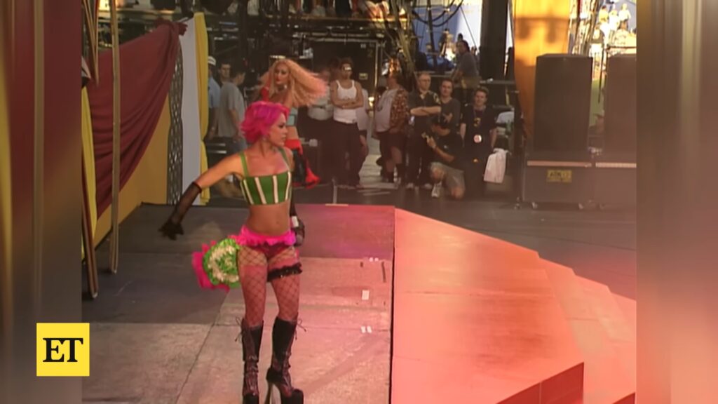Pink‑haired performer in colorful stagewear walks backstage during the 2001 “Lady Marmalade” video shoot.