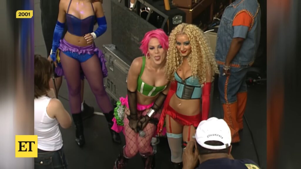 Two performers sing onstage during a 2001 live “Lady Marmalade” performance, wearing colorful early‑2000s costumes.
