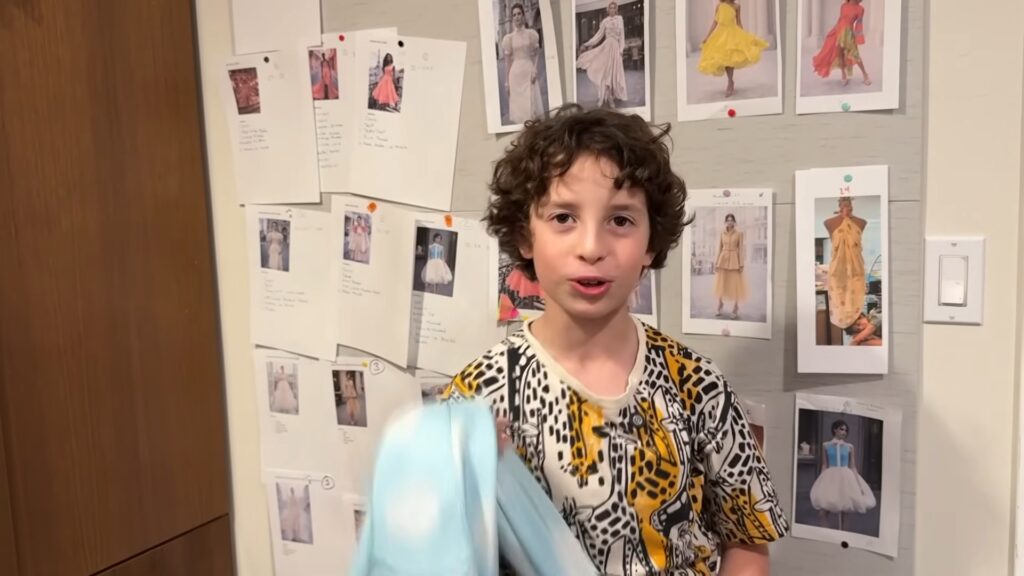 Max Alexander stands in front of a wall of fashion sketches while holding fabric in his studio.