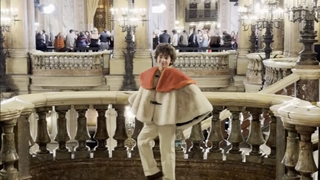 Young designer Max Alexander poses on a marble staircase at a historic Paris Fashion Week location.