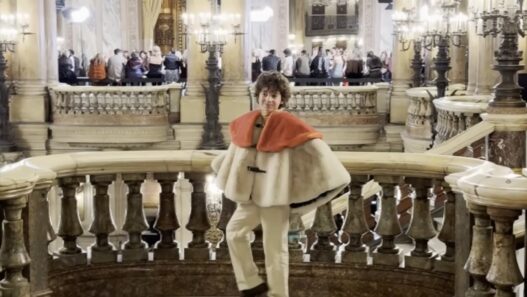 Young designer Max Alexander poses on a marble staircase at a historic Paris Fashion Week location.