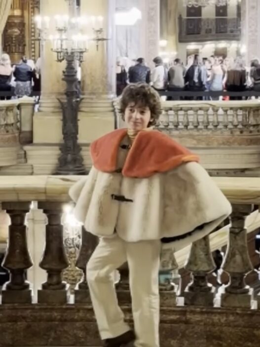 Young designer Max Alexander poses on a marble staircase at a historic Paris Fashion Week location.