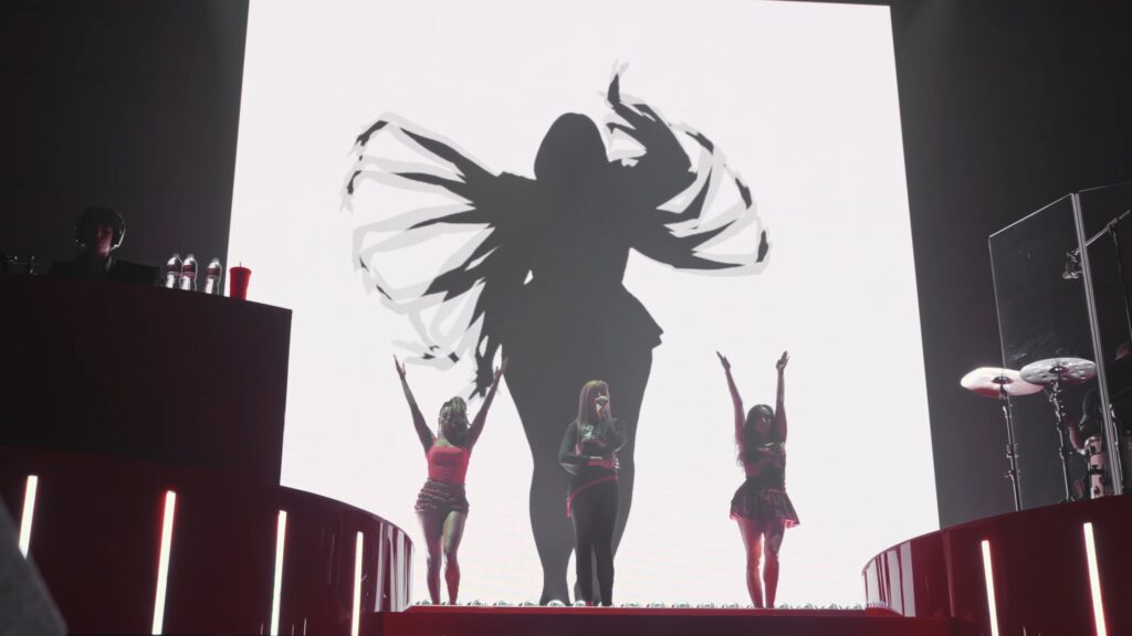 PinkPantheress performing at the Wiltern with dancers in red as a dramatic silhouette fills the stage screen.
