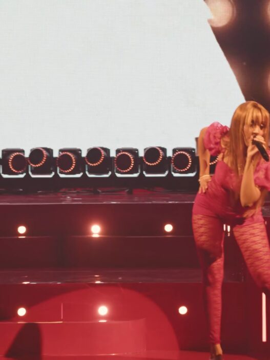 PinkPantheress performing in a bright pink outfit onstage at the Wiltern, surrounded by circular lights and live band setup.