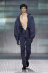 Look from AAA STUDIO’s “Señora, Suélteme El Brazo” runway collection.. Male model on a runway wearing a navy blue oversized hoodie with ruffled trim, unzipped at the chest, and matching joggers with drawstrings.