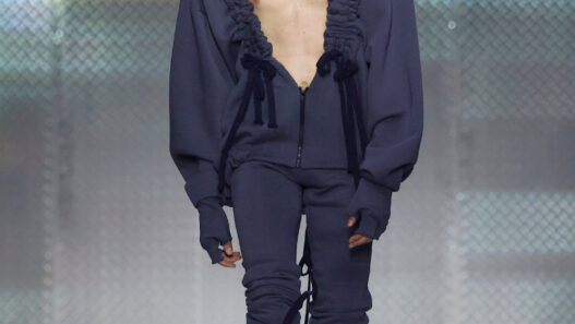 Look from AAA STUDIO’s “Señora, Suélteme El Brazo” runway collection.. Male model on a runway wearing a navy blue oversized hoodie with ruffled trim, unzipped at the chest, and matching joggers with drawstrings.