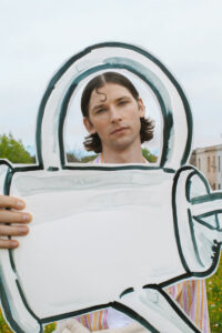 Young man outdoors holding a large white cardboard cutout shaped like a teal-outlined key