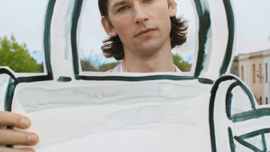 Young man outdoors holding a large white cardboard cutout shaped like a teal-outlined key