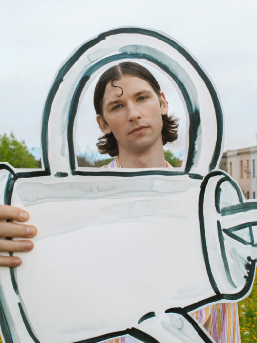 Young man outdoors holding a large white cardboard cutout shaped like a teal-outlined key