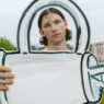 Young man outdoors holding a large white cardboard cutout shaped like a teal-outlined key