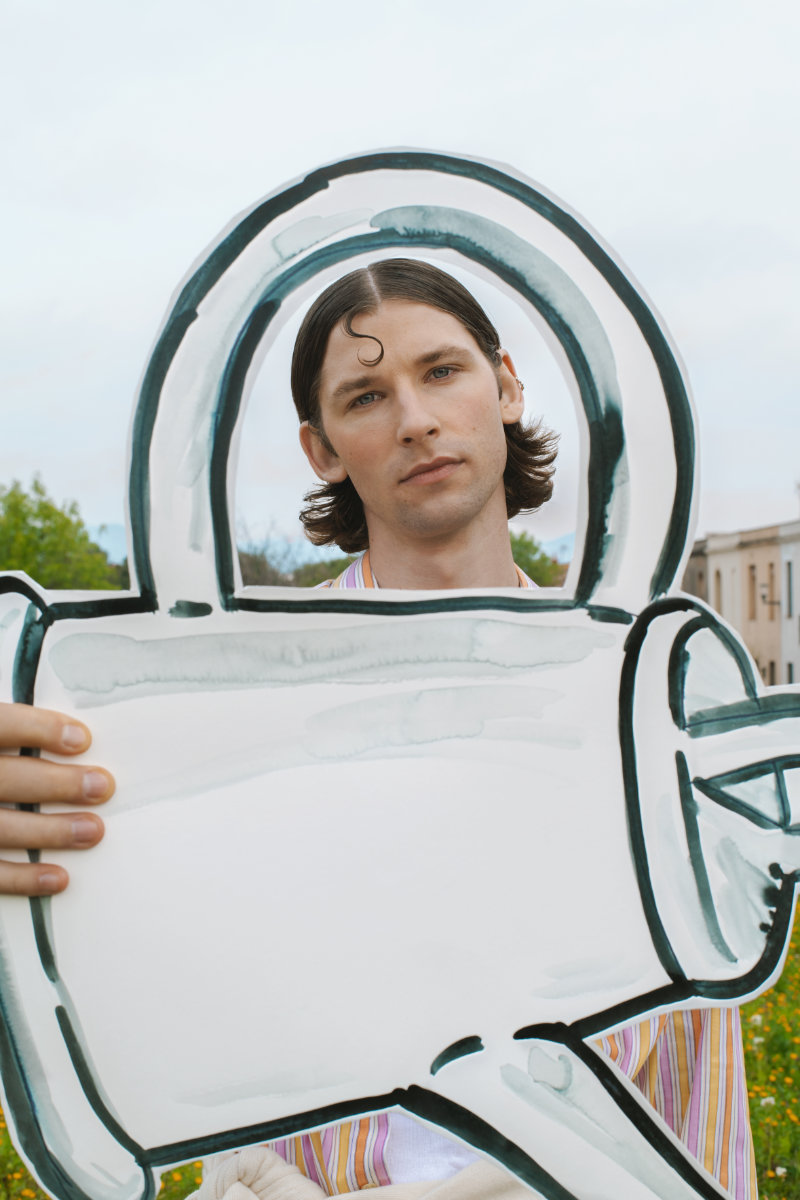 Young man outdoors holding a large white cardboard cutout shaped like a teal-outlined key