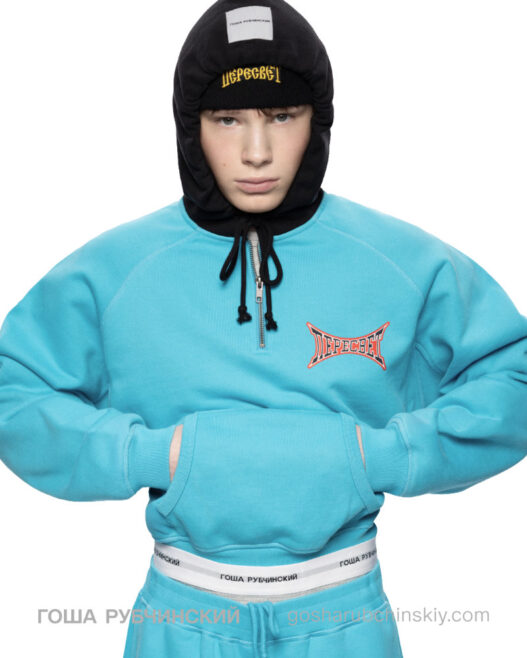 Model wearing a turquoise hoodie and pants with a black hooded balaclava; branded chest logo visible. Gosha Rubchinskiy unveils his bold new “PERESVET” campaign exploring athletic form.vGosha Rubchinskiy unveils his bold new “PERESVET” campaign exploring athletic form. Gosha Rubchinskiy unveils his bold new “PERESVET” campaign exploring athletic form.