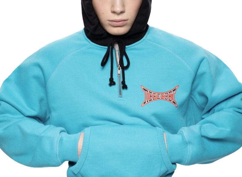 Model wearing a turquoise hoodie and pants with a black hooded balaclava; branded chest logo visible. Gosha Rubchinskiy unveils his bold new “PERESVET” campaign exploring athletic form.vGosha Rubchinskiy unveils his bold new “PERESVET” campaign exploring athletic form. Gosha Rubchinskiy unveils his bold new “PERESVET” campaign exploring athletic form.