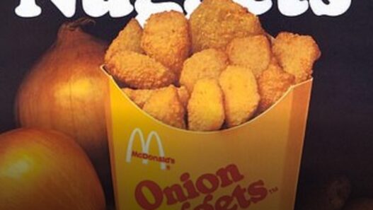 Box of McDonald's Onion Nuggets overflowing with nuggets, with a bold article headline about why McDonald's doesn’t have onion rings like Burger King in the foreground.