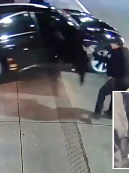 Surveillance image of a black SUV with its door open and a person standing near the driver's side on a sidewalk area outside a store.