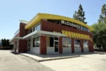 Exterior view of a McDonald's restaurant with a yellow roof, red brick walls, and striped awning on a sunny day.