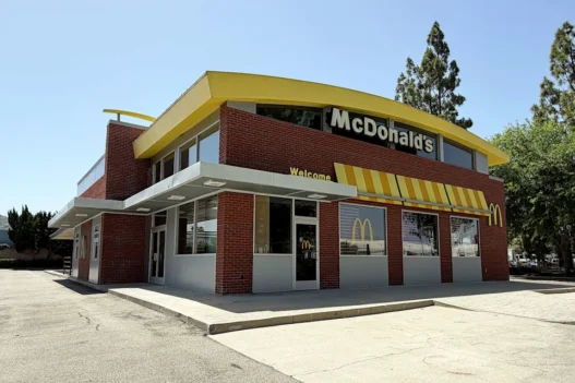 Exterior view of a McDonald's restaurant with a yellow roof, red brick walls, and striped awning on a sunny day.