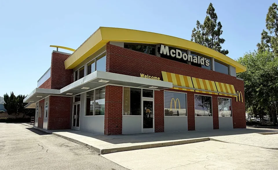 Exterior view of a McDonald's restaurant with a yellow roof, red brick walls, and striped awning on a sunny day.