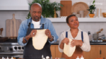 Two people in a bright kitchen, each tossing dough into the air as they cook together.