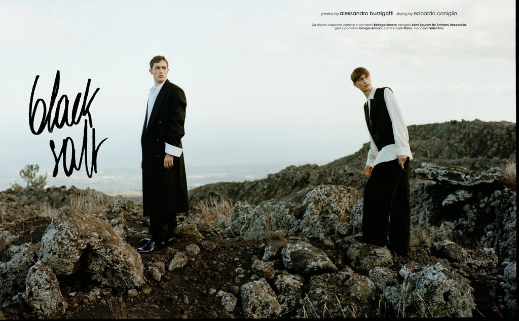 Two male models in black-and-white outfits pose on rocky terrain for a fashion editorial, with a handwritten 'look' graphic on the left.