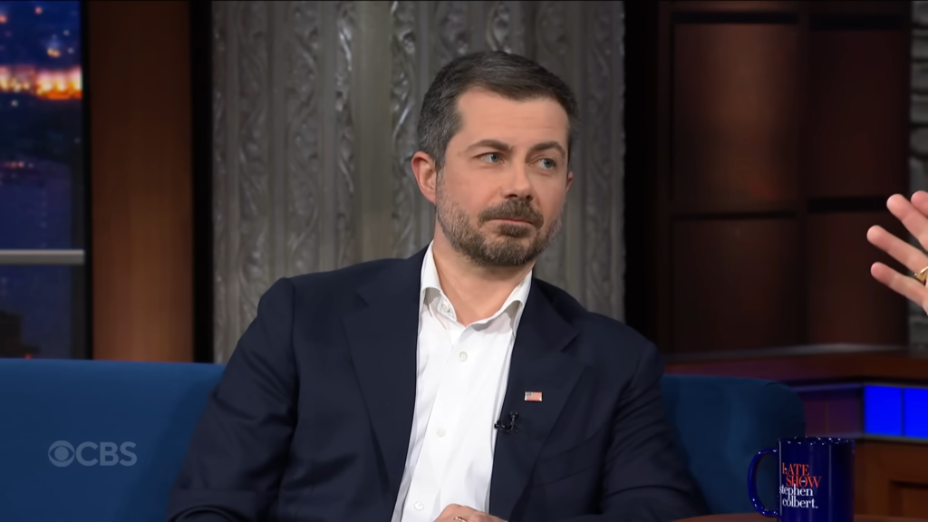 Man in a navy suit on a late-night talk show set, with a hand gesture visible and a CBS watermark in the corner.