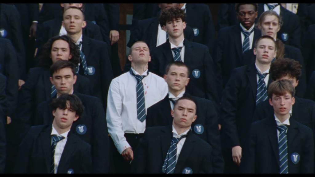 Group of young men in dark blazers and striped ties standing together, blue badges on lapels visible.
