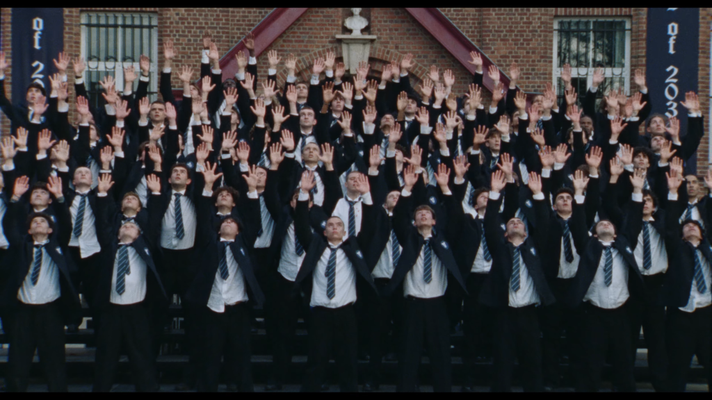 Large group of men in suits raising their hands in unison in front of a brick building during a ceremony or photo.