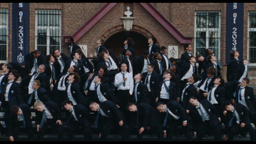 Large group of students in navy blazers and striped ties standing and leaning on steps outside a brick building with an arched entrance and banners visible in the background.