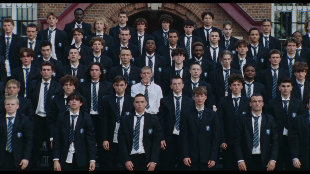 Group of students in dark blazers and striped ties posing on steps outside a brick building for a school photo