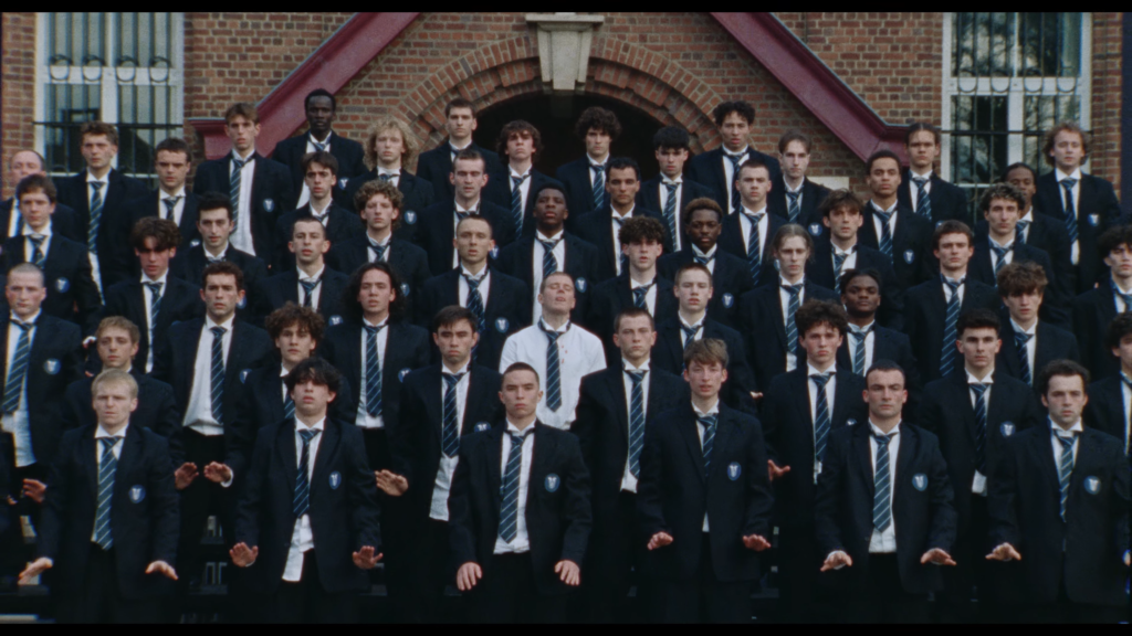 Large group of male students in navy blazers and striped ties posing for a class photo outside a brick building.