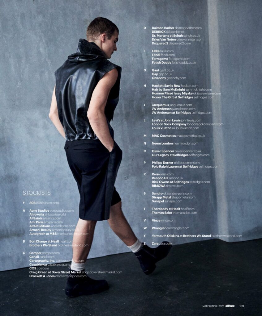 Model in a sleeveless black leather vest and black shorts stands with a blue-gray studio wall, large stockist list to the right labeled STOCKISTS.