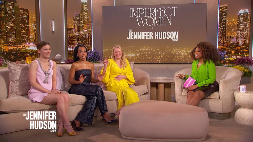 Four women sit on a beige sofa on a TV talk show set with a city skyline backdrop and 'Imperfect Women' logo visible behind them on a large screen.