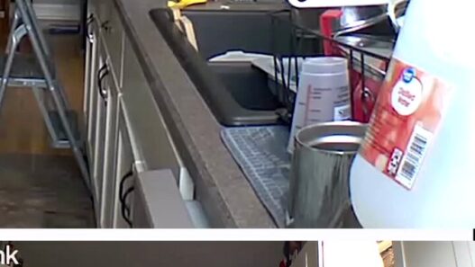 Cluttered kitchen with white cabinets, a stainless sink, a green dish rack, and a step ladder in the center.