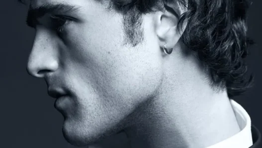 Side profile of a young man in a suit, wearing a hoop earring, in a moody black-and-white portrait.