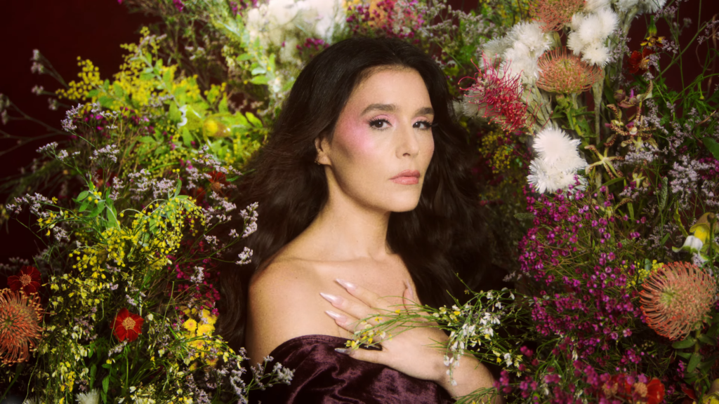 Portrait of a woman surrounded by a lush arrangement of colorful flowers, gazing softly at the camera.
