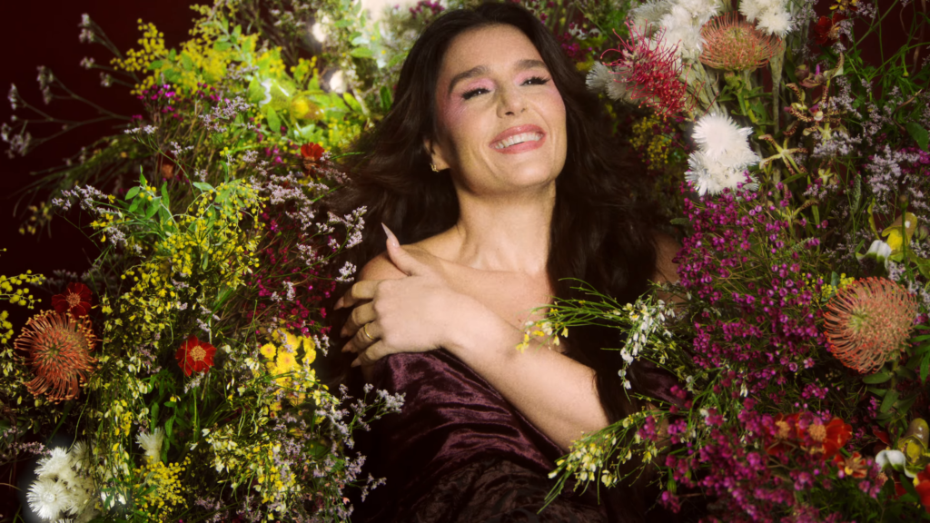 Smiling woman lies among a vibrant bouquet of wildflowers, arms crossed over her chest.