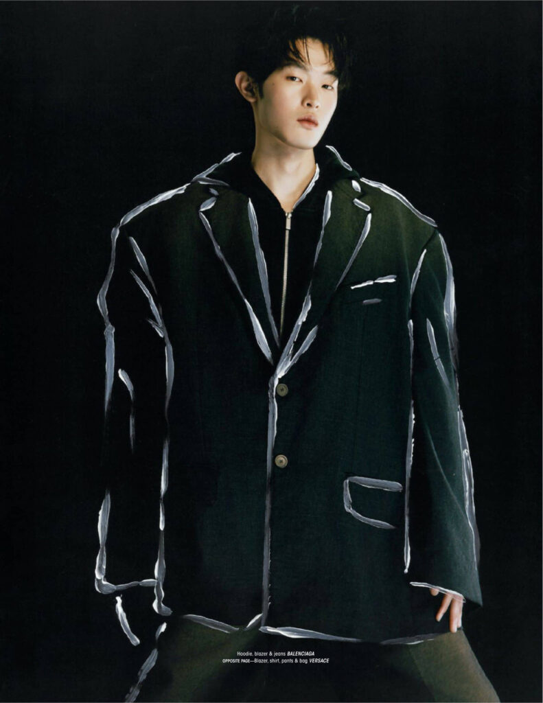 Male model in a dark blazer with white brushstroke patterns against a black background, fashion editorial.