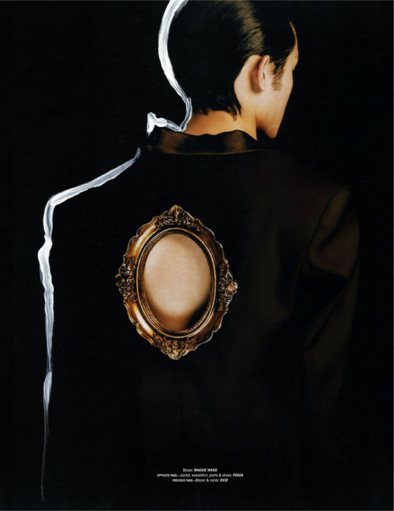 Person seen from behind wearing a black blazer with an ornate gold oval mirror patch on the back; white ribbon trails along the shoulder area.