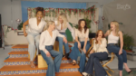 Group of women in white tops and jeans sitting and laughing on decorative tiled stairs in a studio backdrop with greenery and flowers behind them (People logo in corner).