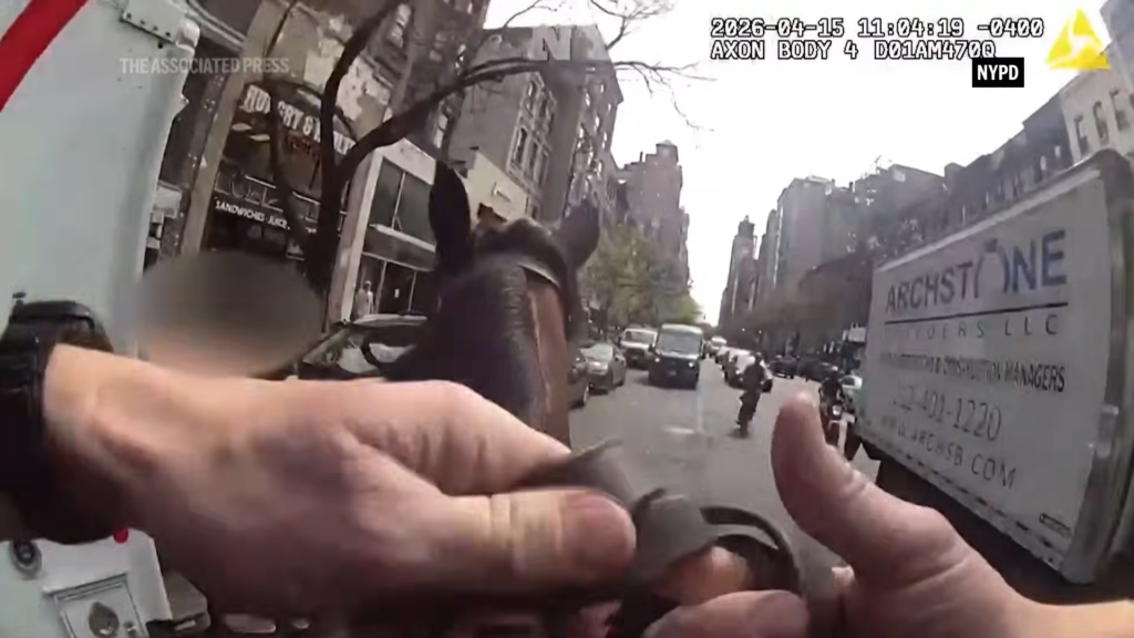 First-person view from a mounted NYPD officer’s body camera on a city street; hands adjust gear as a horse and rider advance past parked cars.
