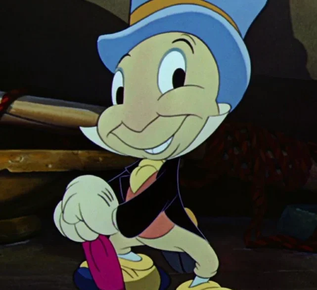 Cheerful Pinocchio-like cartoon boy in a blue hat and yellow shoes, smiling and pointing, while holding a pink umbrella.