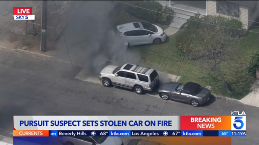 Aerial view of a silver SUV smoking as it sits on a residential street, breaking news banner at bottom reading 'Pursuit Suspect Sets Stolen Car on Fire'.